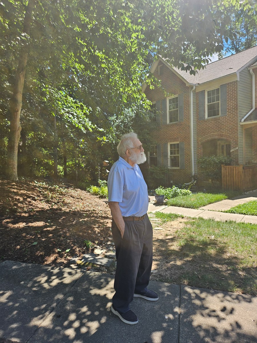 Grandfather standing outdoors looking upward beneath trees