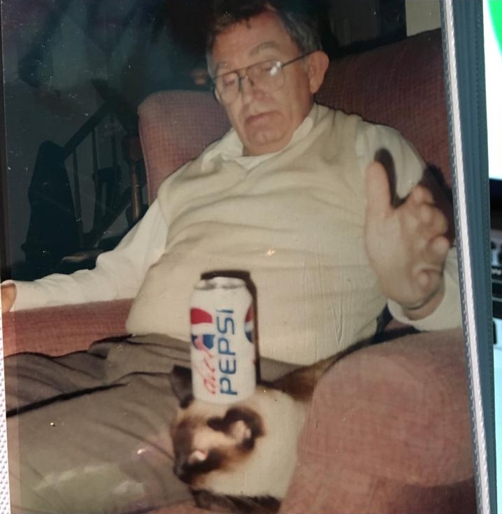 A vintage photograph of grandfather seated in a chair beside a cat and a cola can
