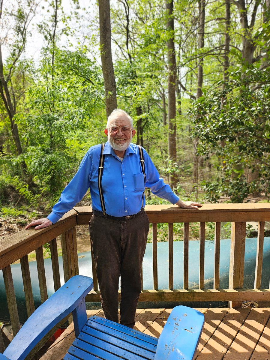 Grandfather smiling beside a deck railing with trees behind him