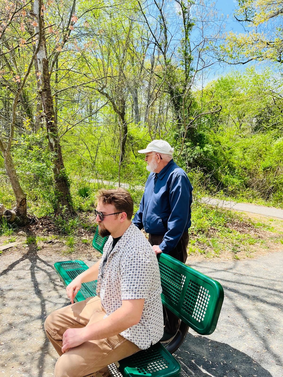 Two people beside a green bench on a tree-lined path