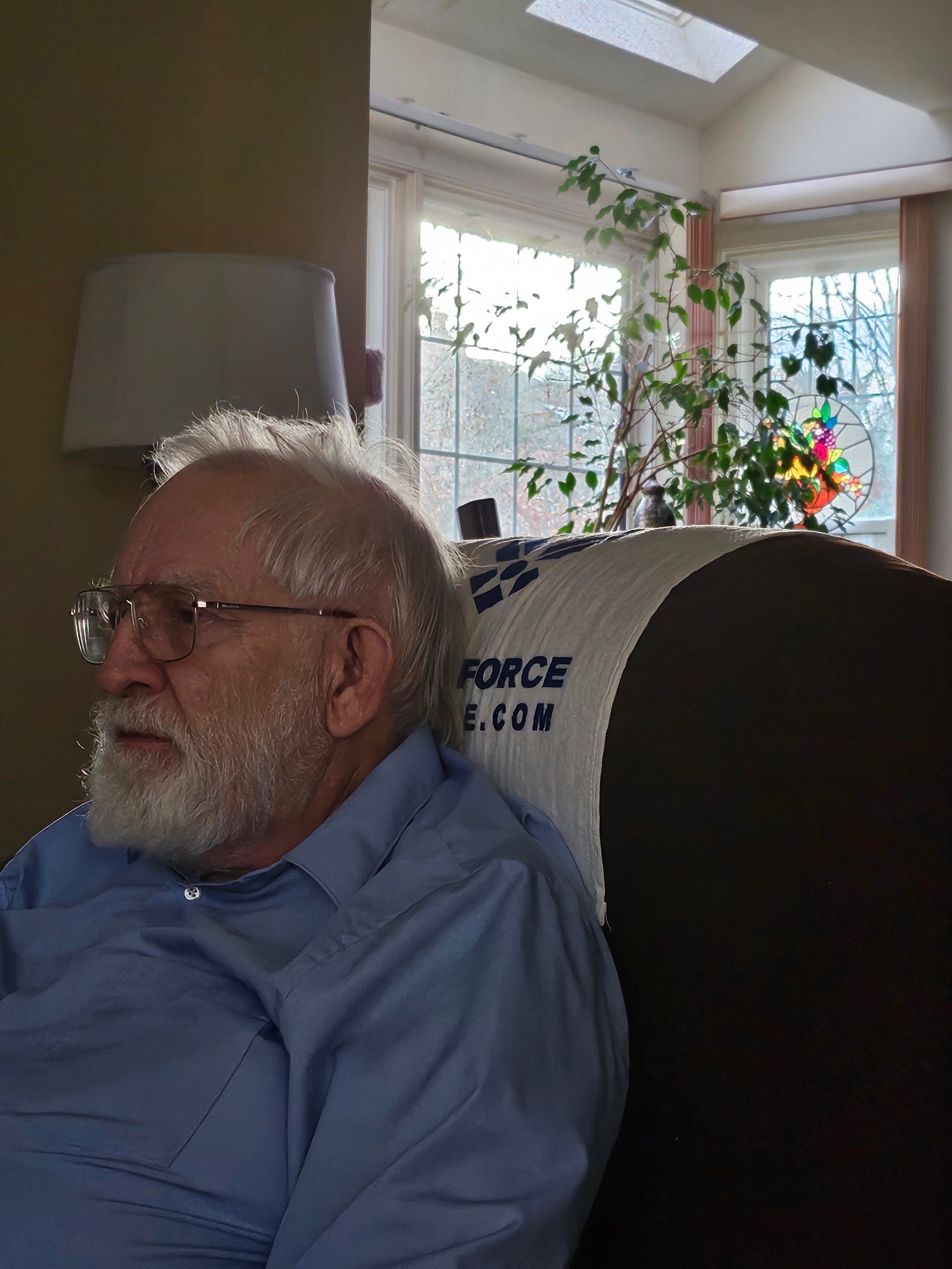 Grandfather seated in a blue shirt beside a window