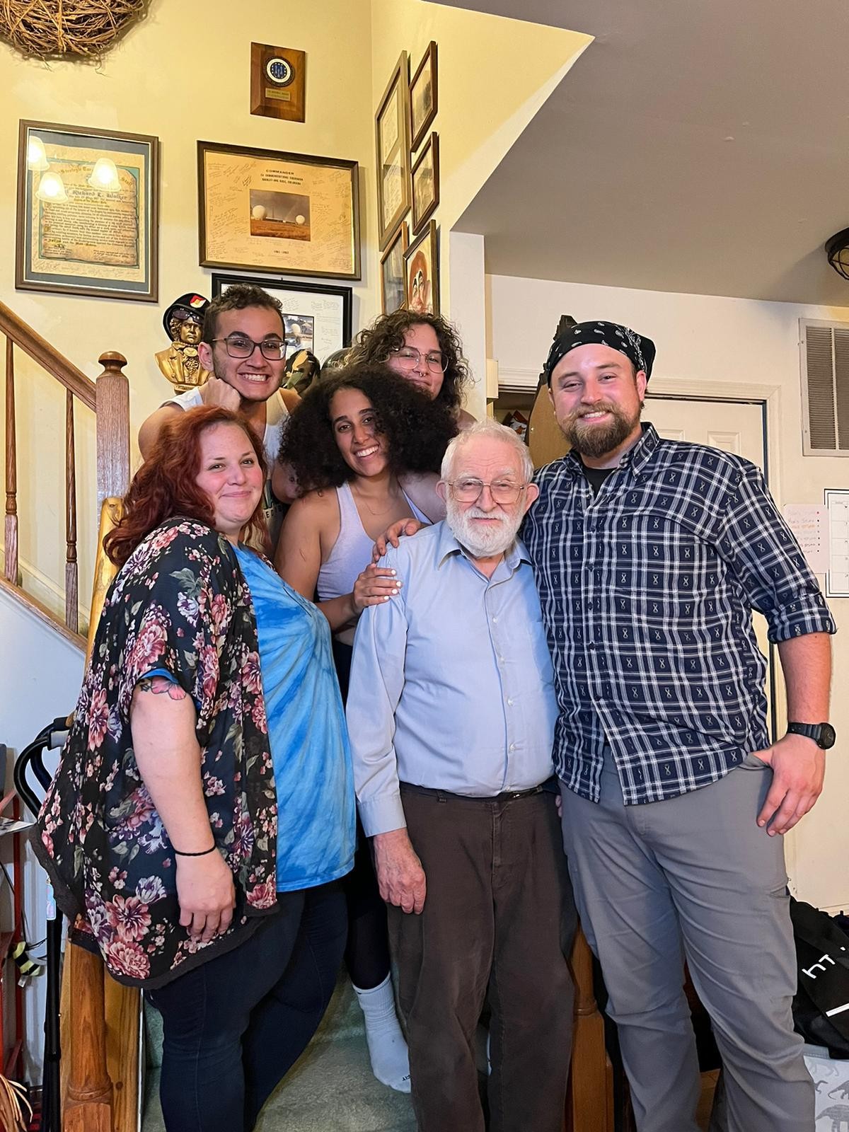 Six people smiling together indoors beside a staircase