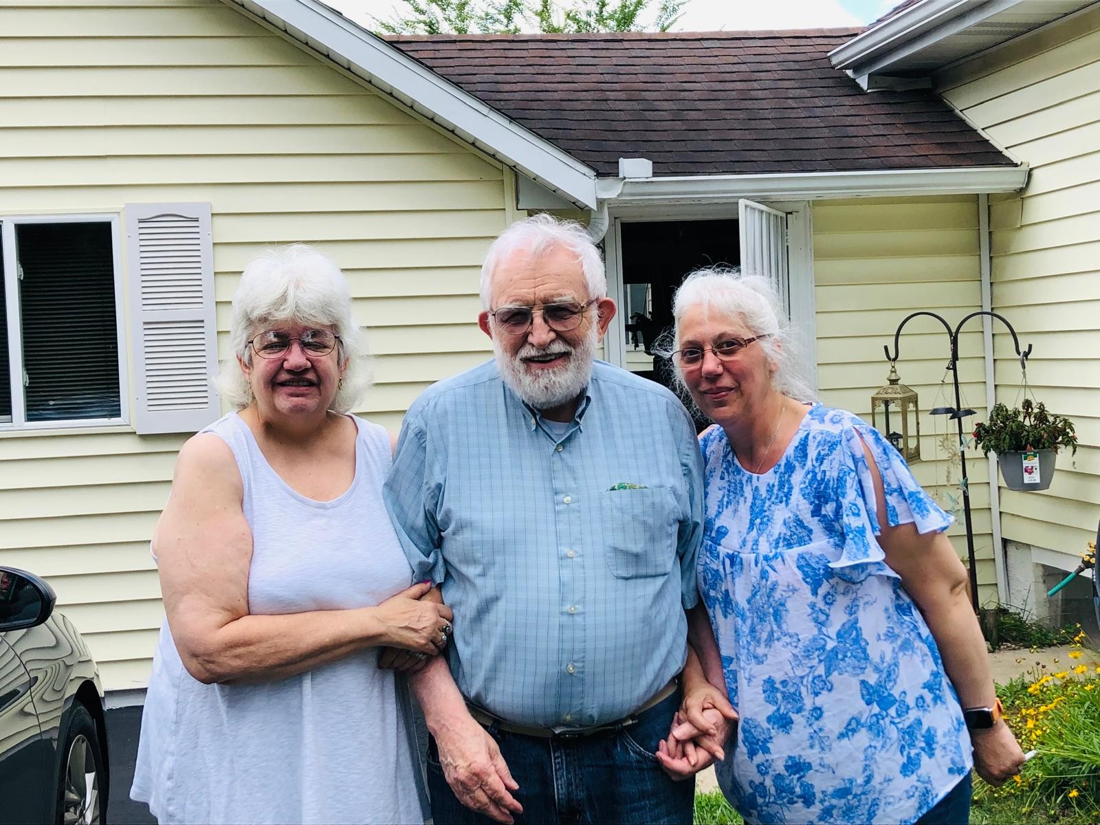 Three people standing together outside a yellow house
